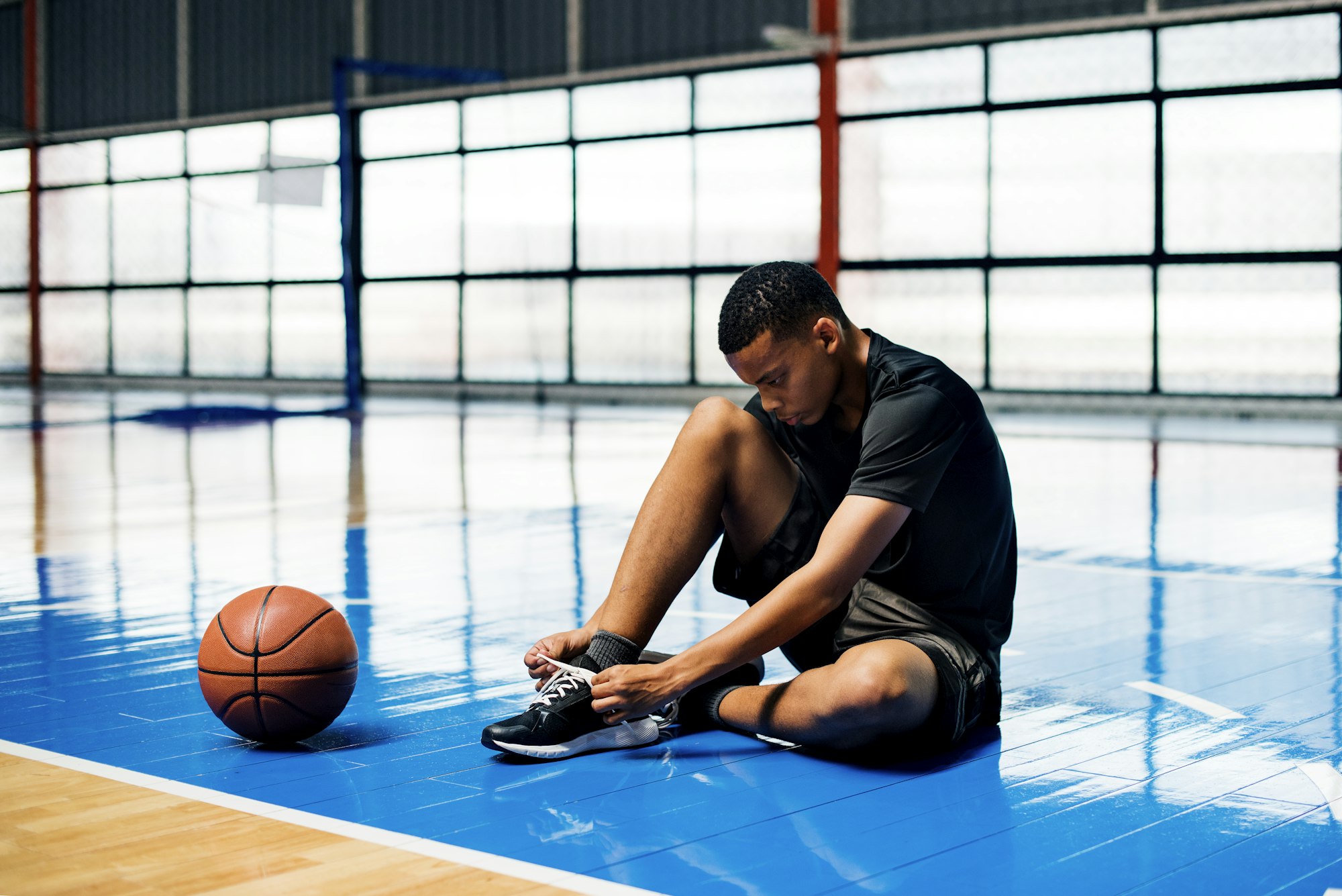 African American teenage boy tying his shoe laces on a basketball court